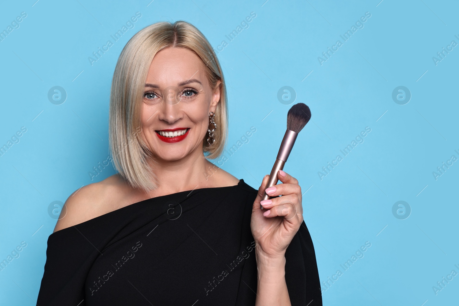 Photo of Smiling woman with makeup brush on light blue background