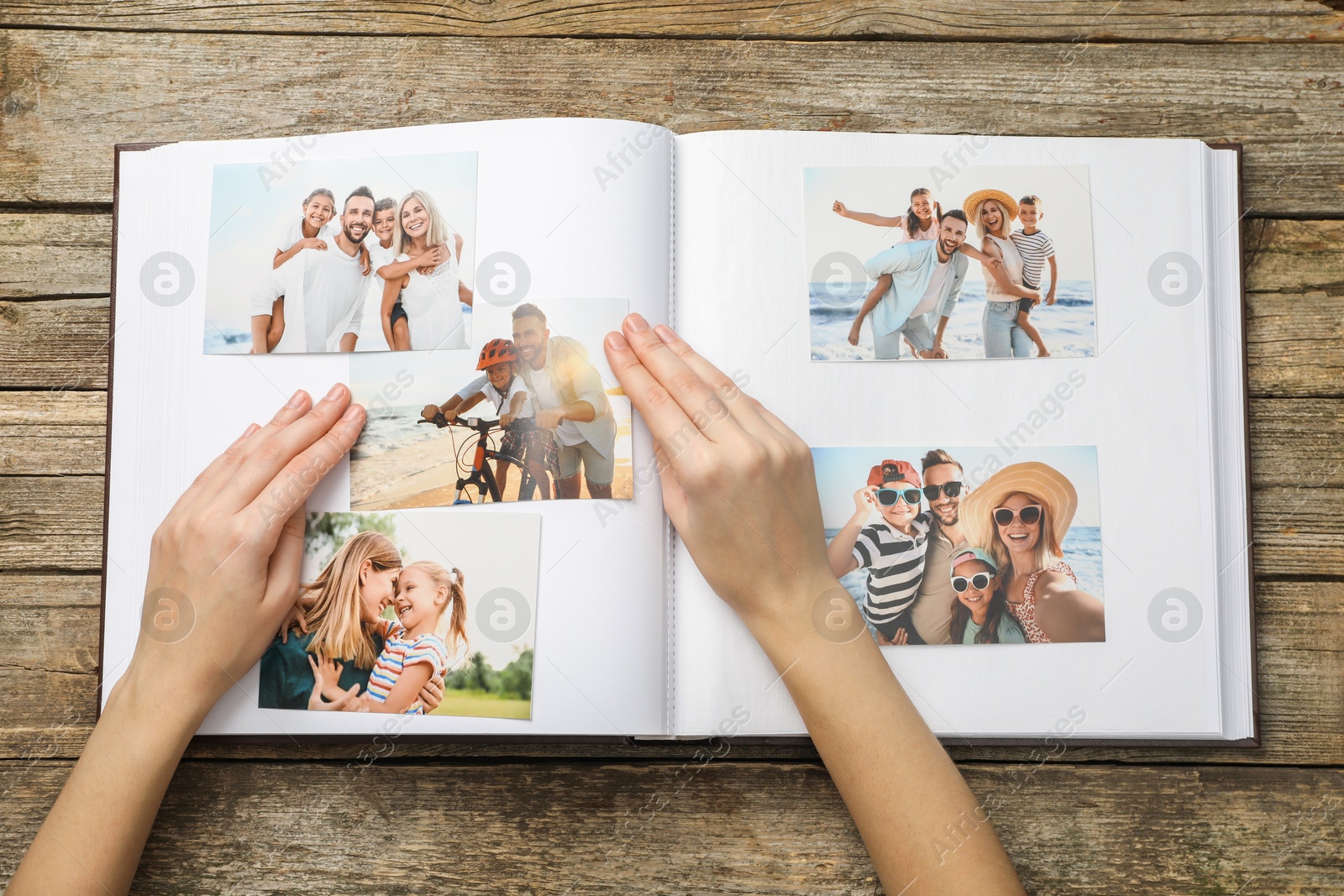 Photo of Woman with different photos in open photo album at wooden table, top view