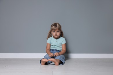 Photo of Orphanage concept. Sad little girl sitting on floor near grey wall