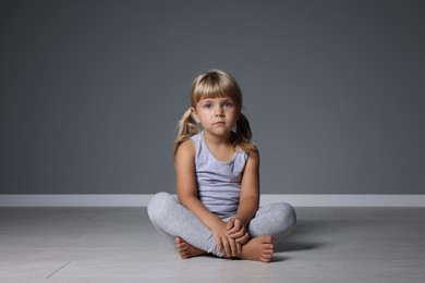 Photo of Orphanage concept. Sad little girl sitting on floor near grey wall