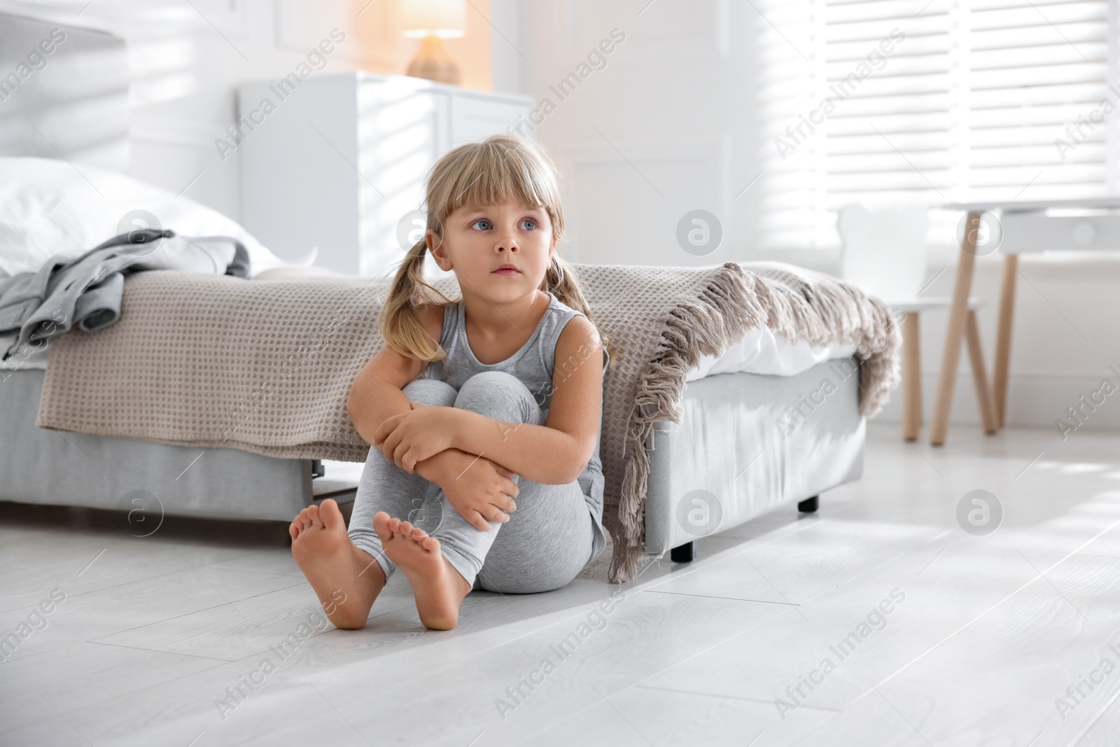 Photo of Orphanage concept. Sad little girl sitting on floor in child`s room