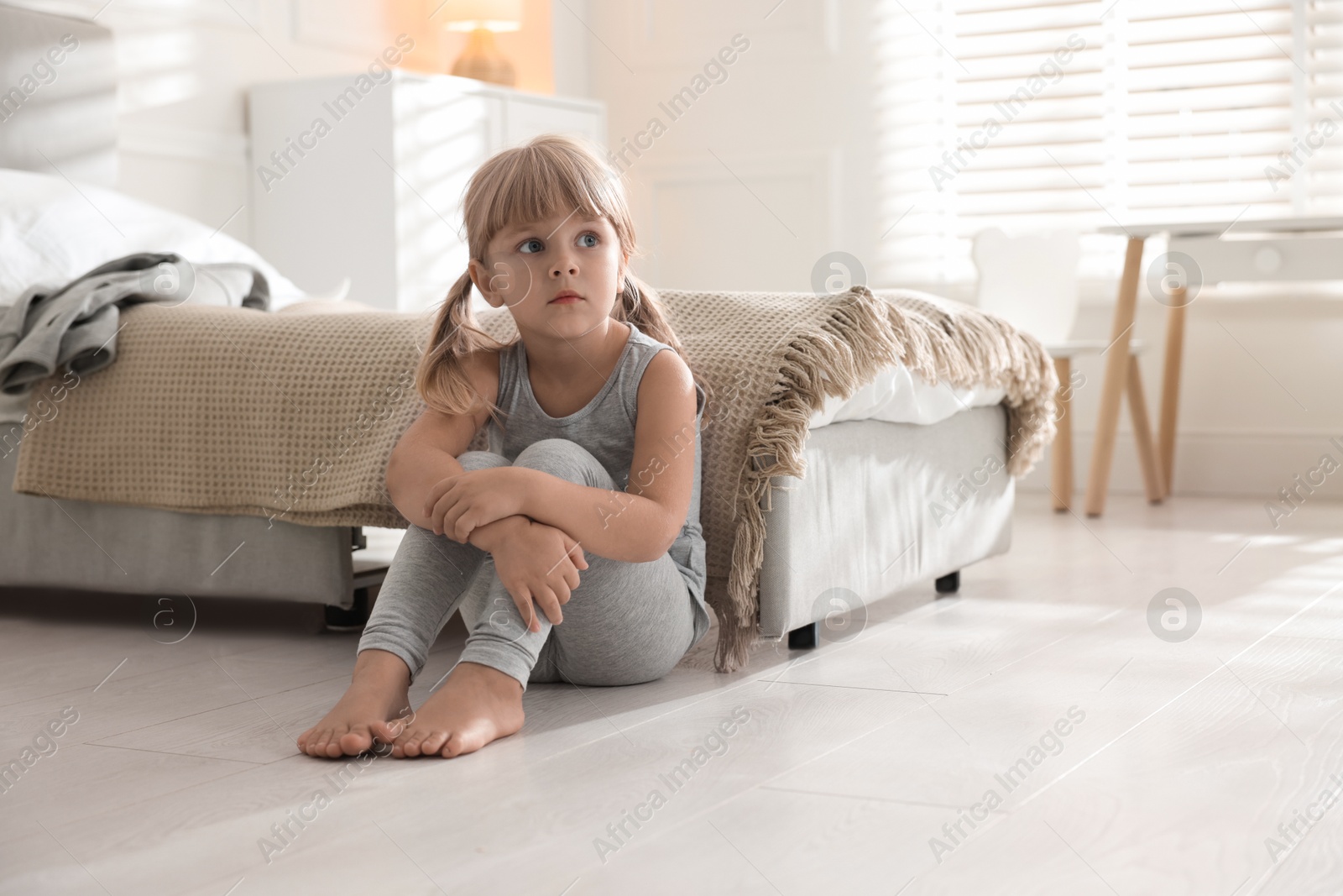 Photo of Orphanage concept. Sad little girl sitting on floor in child`s room