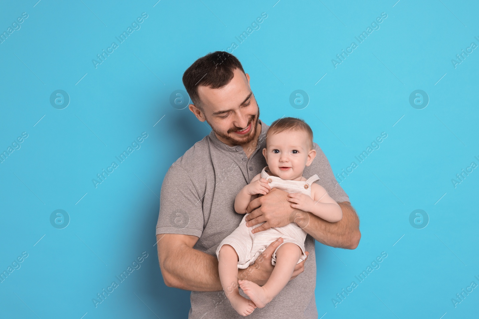 Photo of Father with his cute baby on light blue background