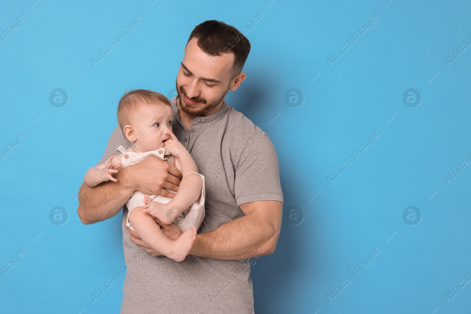 Photo of Father with his cute baby on light blue background, space for text