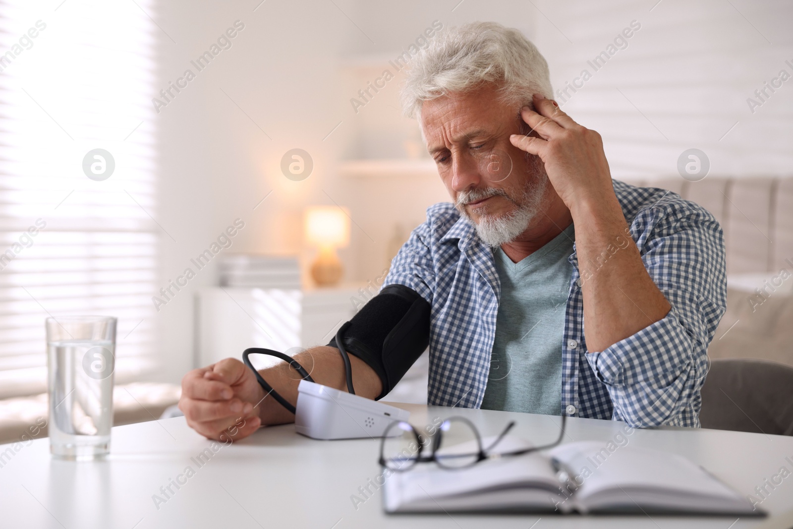 Photo of Senior man measuring blood pressure at table indoors