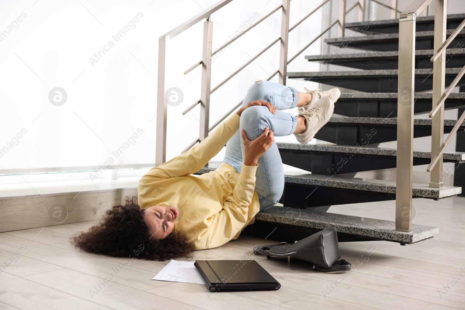 Photo of Woman with injured knee on stairs in building after fall. Dangerous accident