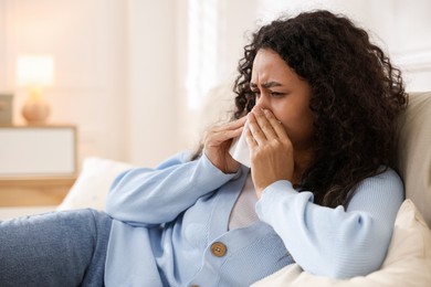 Photo of Young woman with tissue blowing runny nose at home