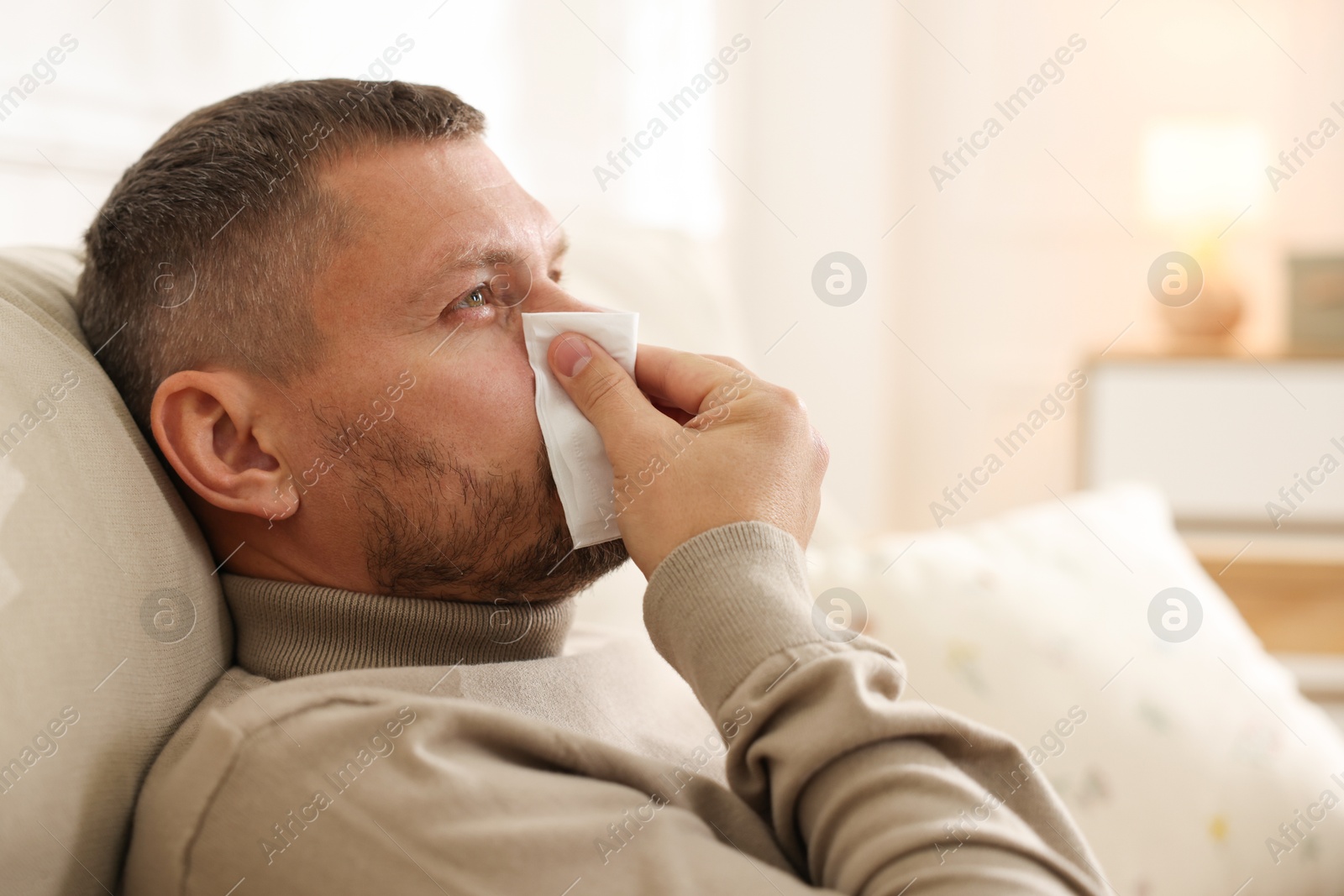 Photo of Man with tissue blowing runny nose at home. Space for text