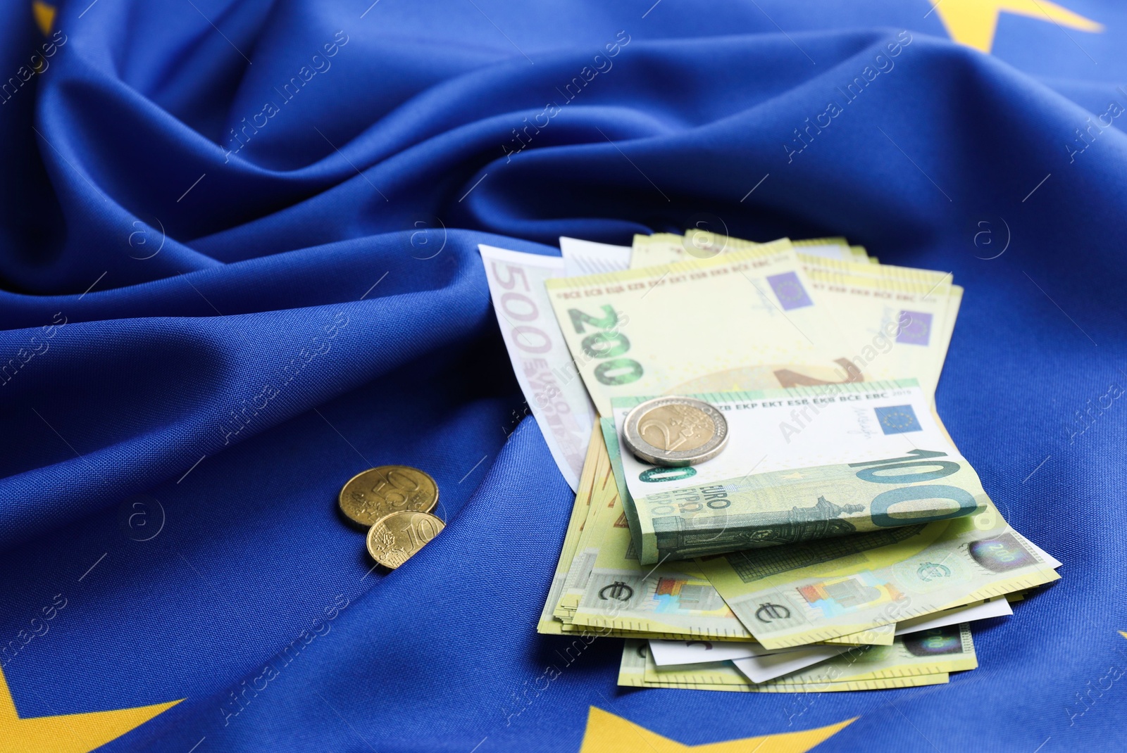 Photo of Euro banknotes and coins on European Union flag, closeup