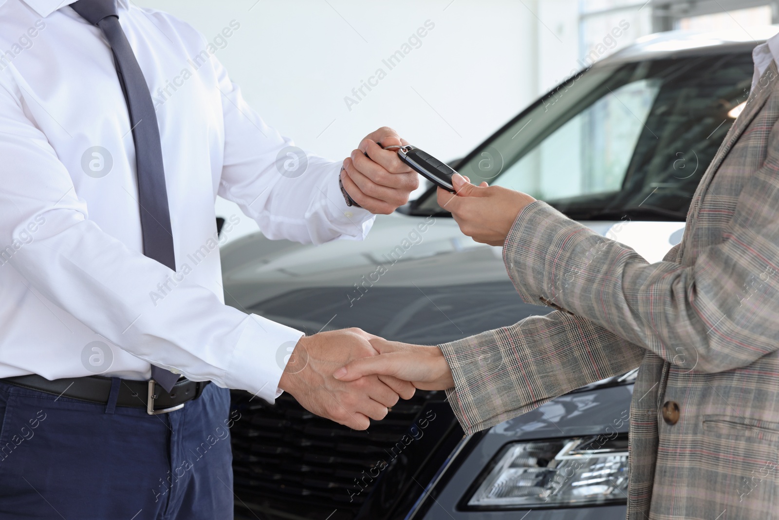 Photo of Salesman giving key to client near new car in salon, closeup