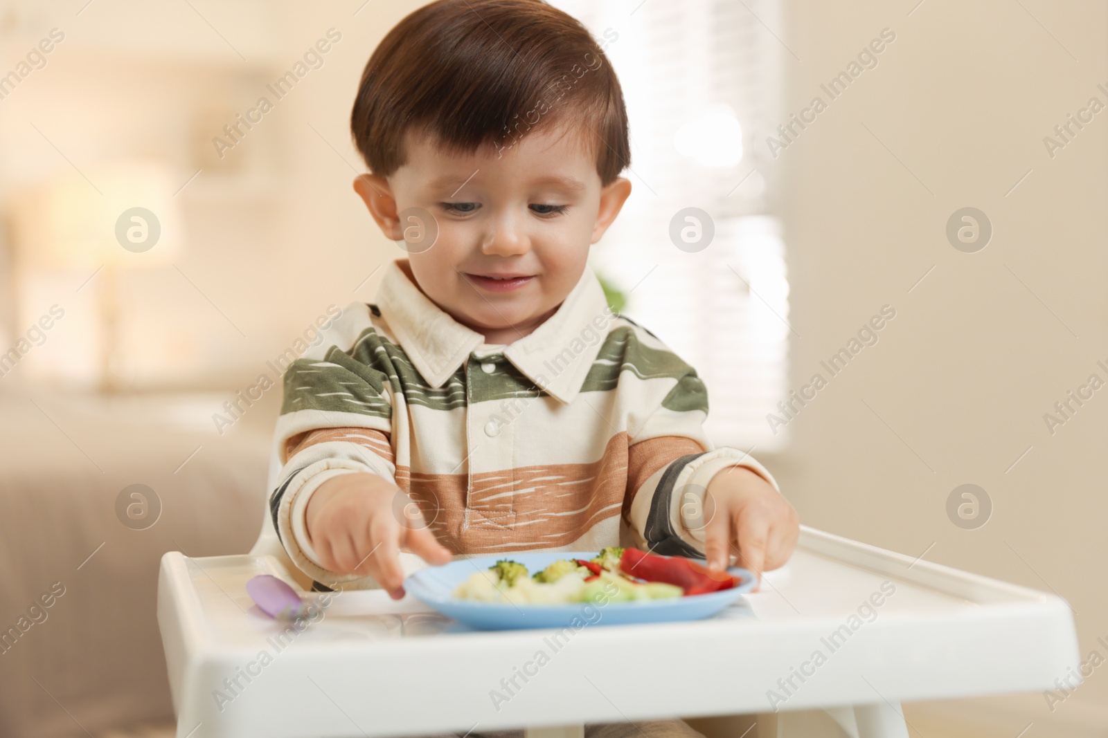 Photo of Cute little baby eating healthy food in high chair at home