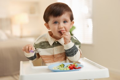 Photo of Cute little baby eating healthy food in high chair at home