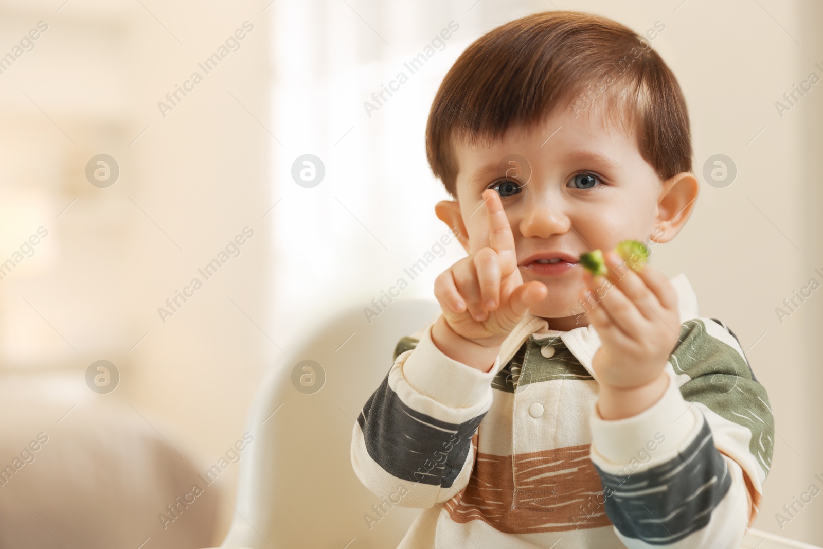 Photo of Cute little baby eating healthy food in high chair at home