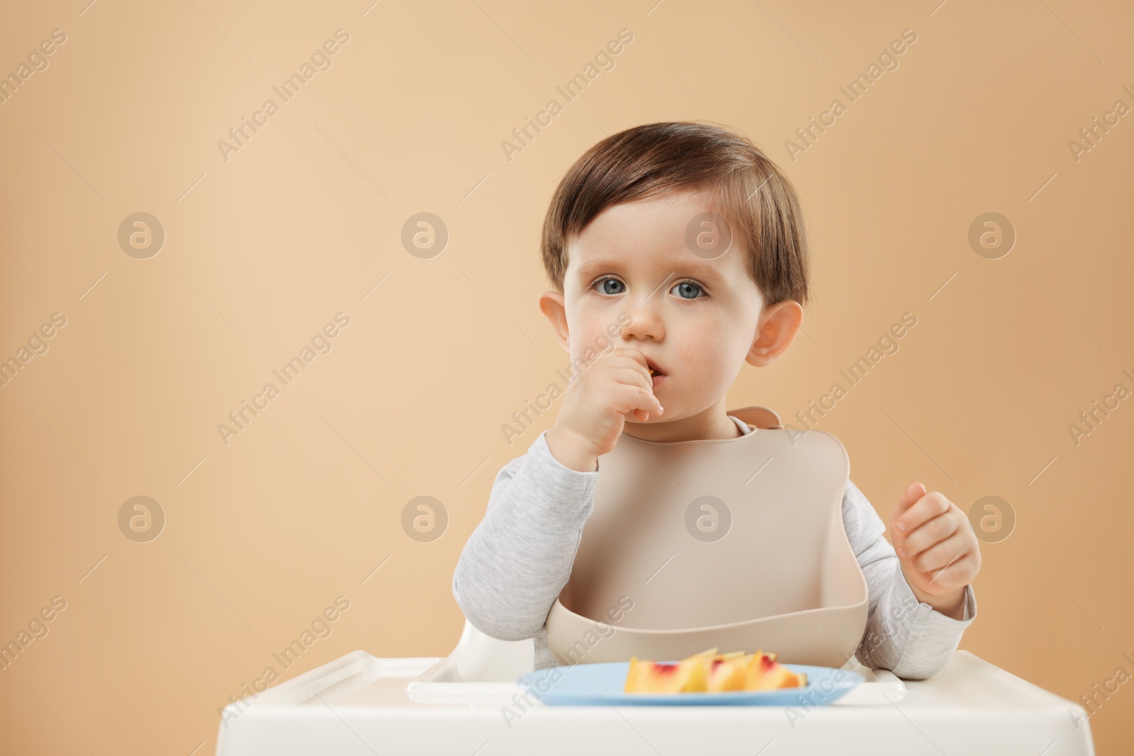 Photo of Healthy baby food. Cute little kid eating fruits in high chair on beige background, space for text