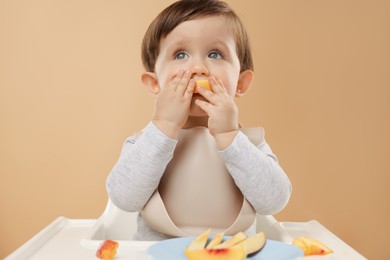 Photo of Healthy baby food. Cute little kid eating fruits in high chair on beige background