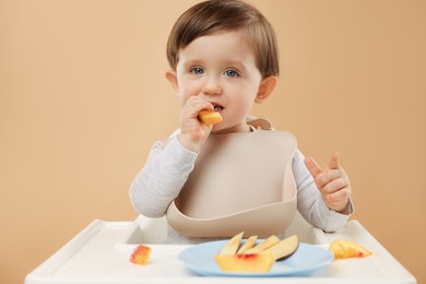 Photo of Healthy baby food. Cute little kid eating fruits in high chair on beige background