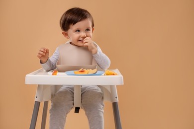 Photo of Healthy baby food. Cute little kid eating fruits in high chair on beige background, space for text