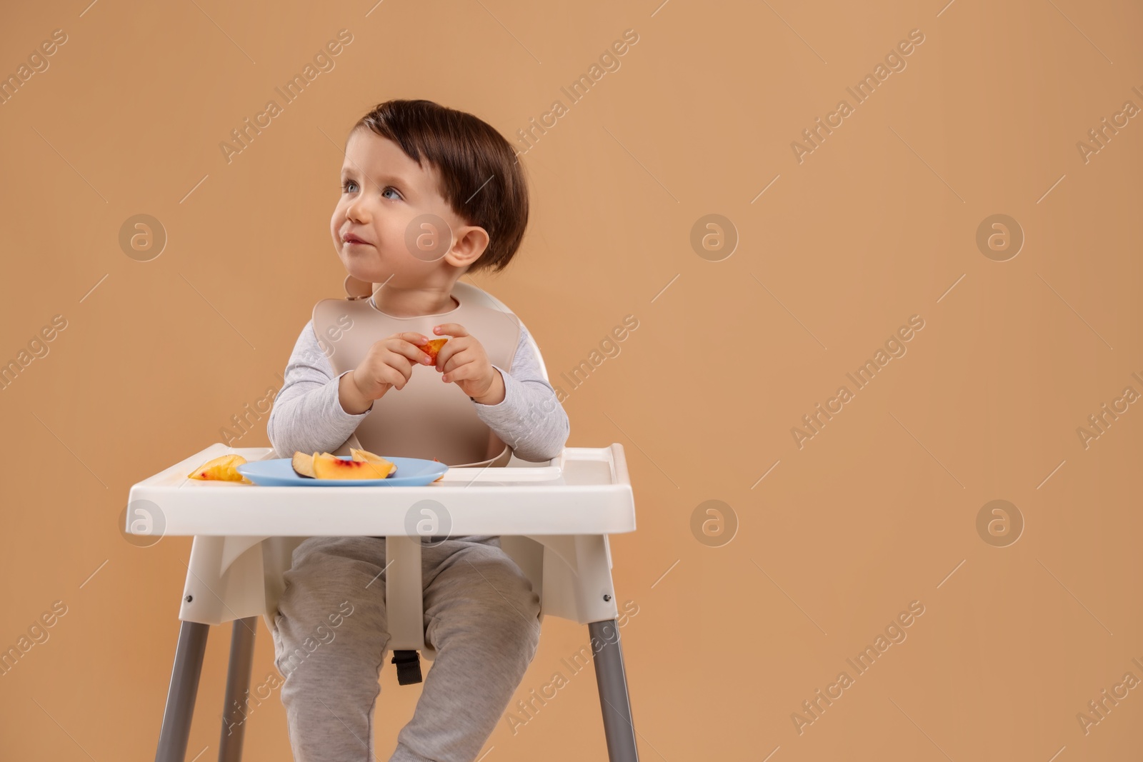 Photo of Healthy baby food. Cute little kid eating fruits in high chair on beige background, space for text