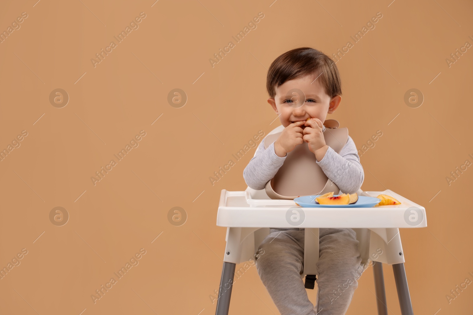 Photo of Healthy baby food. Cute little kid eating fruits in high chair on beige background, space for text