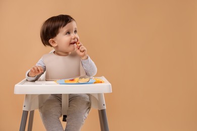 Photo of Healthy baby food. Cute little kid eating fruits in high chair on beige background, space for text