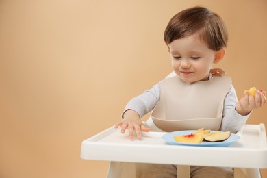 Photo of Healthy baby food. Cute little kid eating fruits in high chair on beige background, space for text