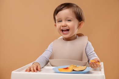 Photo of Healthy baby food. Cute little kid eating fruits in high chair on beige background