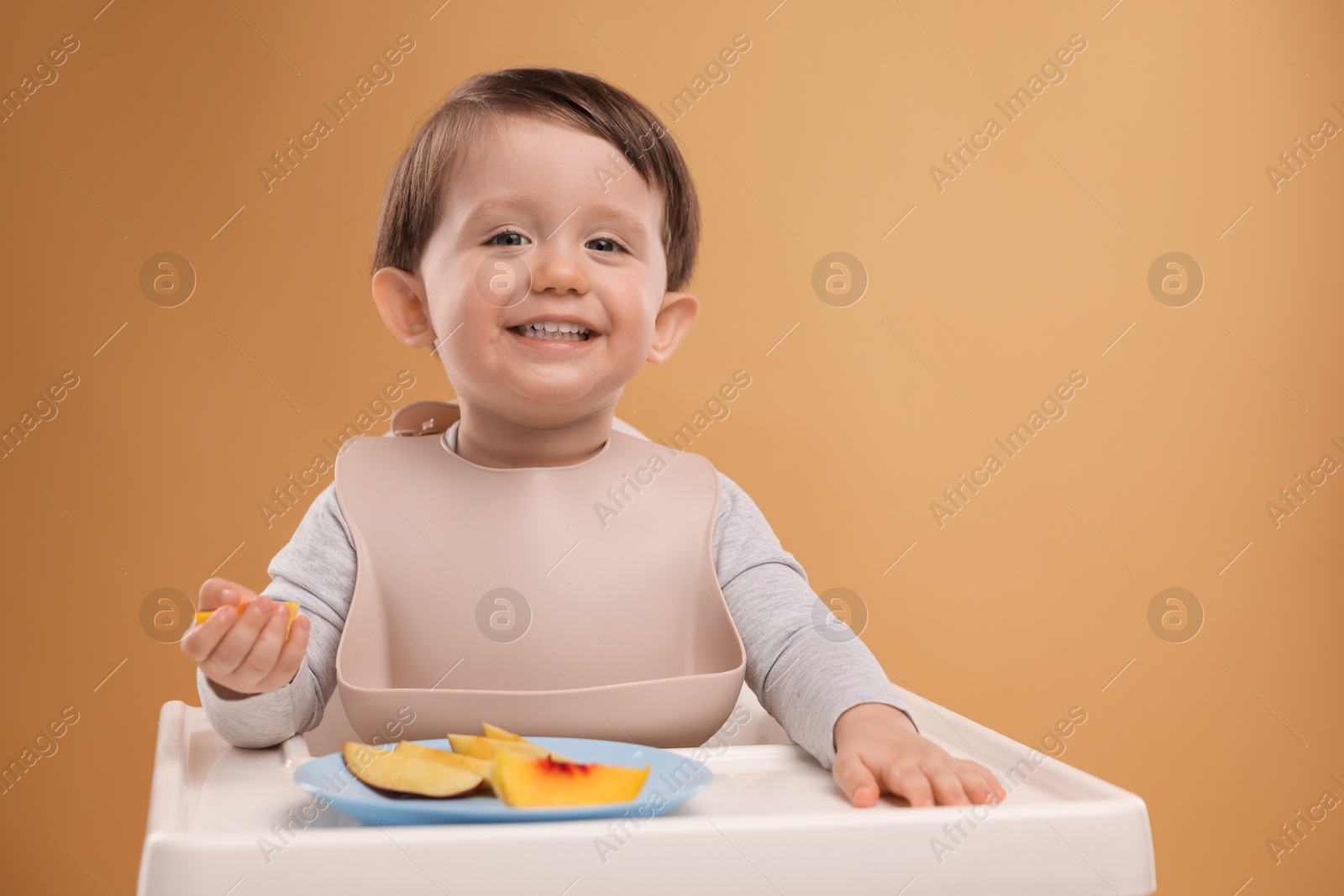 Photo of Healthy baby food. Cute little kid eating fruits in high chair on beige background