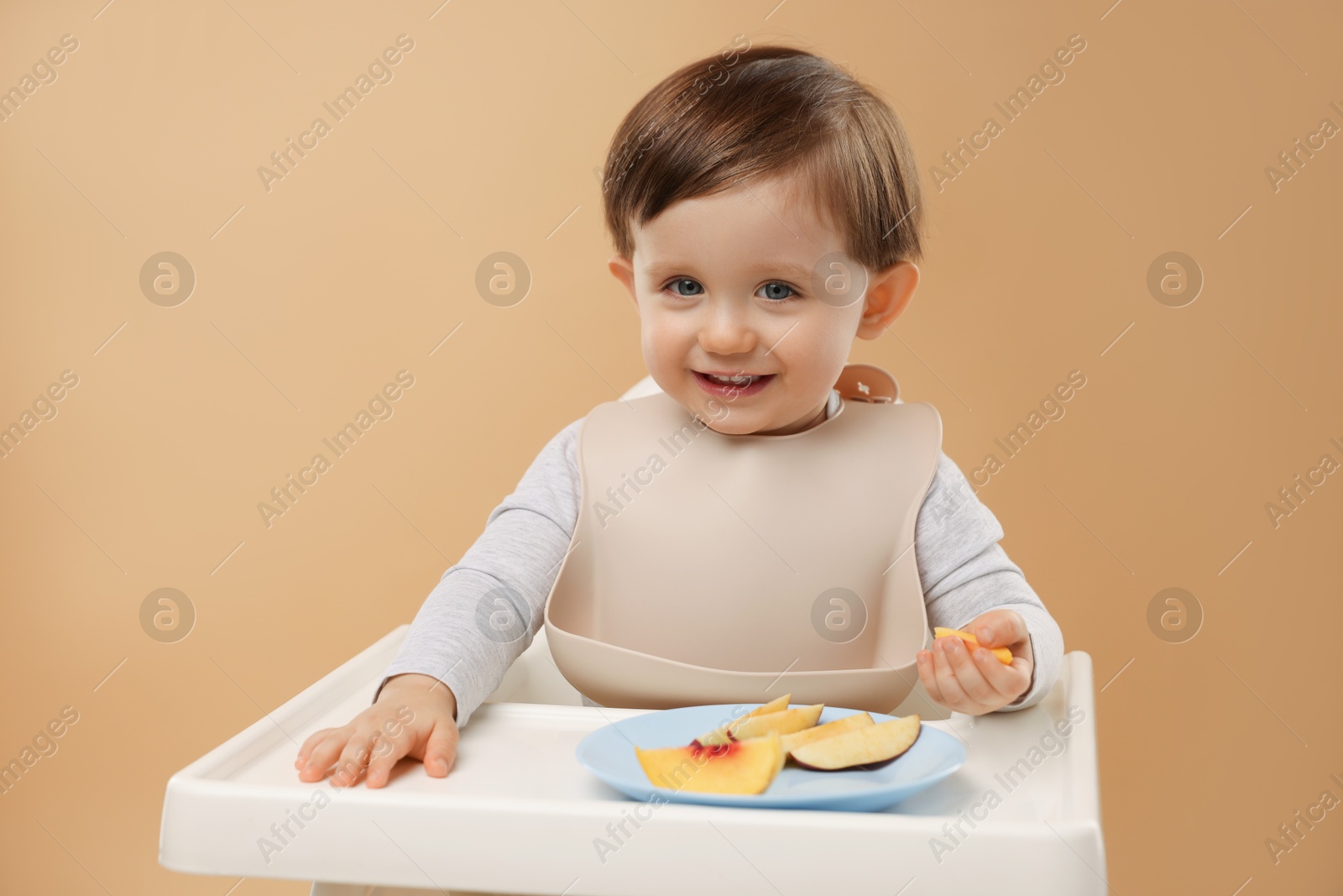 Photo of Healthy baby food. Cute little kid eating fruits in high chair on beige background