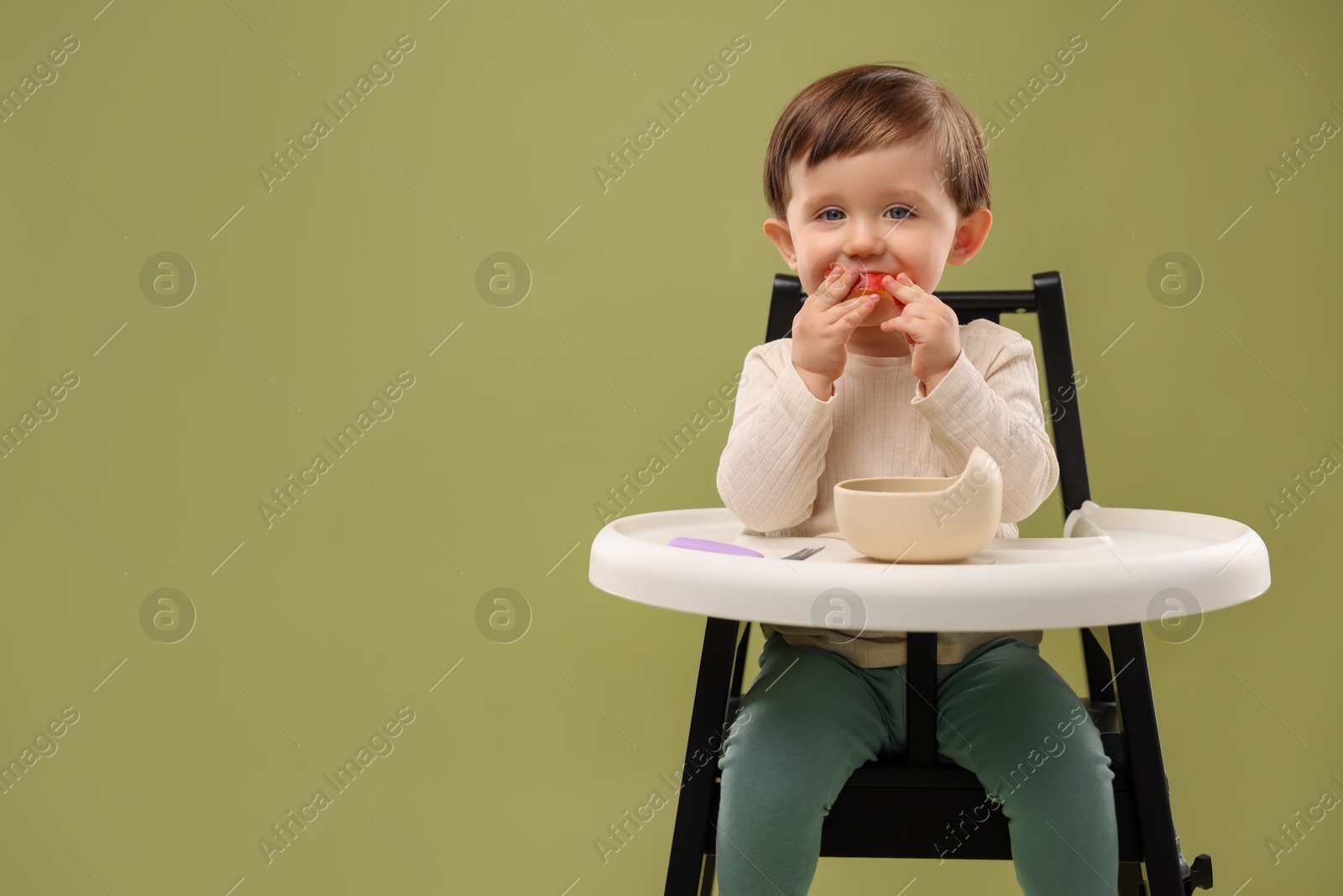 Photo of Cute little baby eating healthy food from bowl in high chair on olive background, space for text