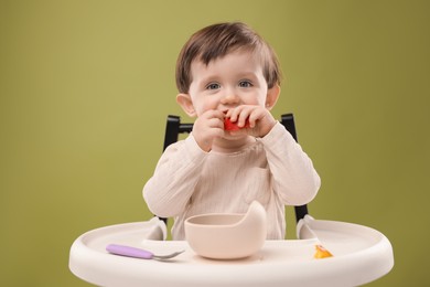 Photo of Cute little baby eating healthy food from bowl in high chair on olive background