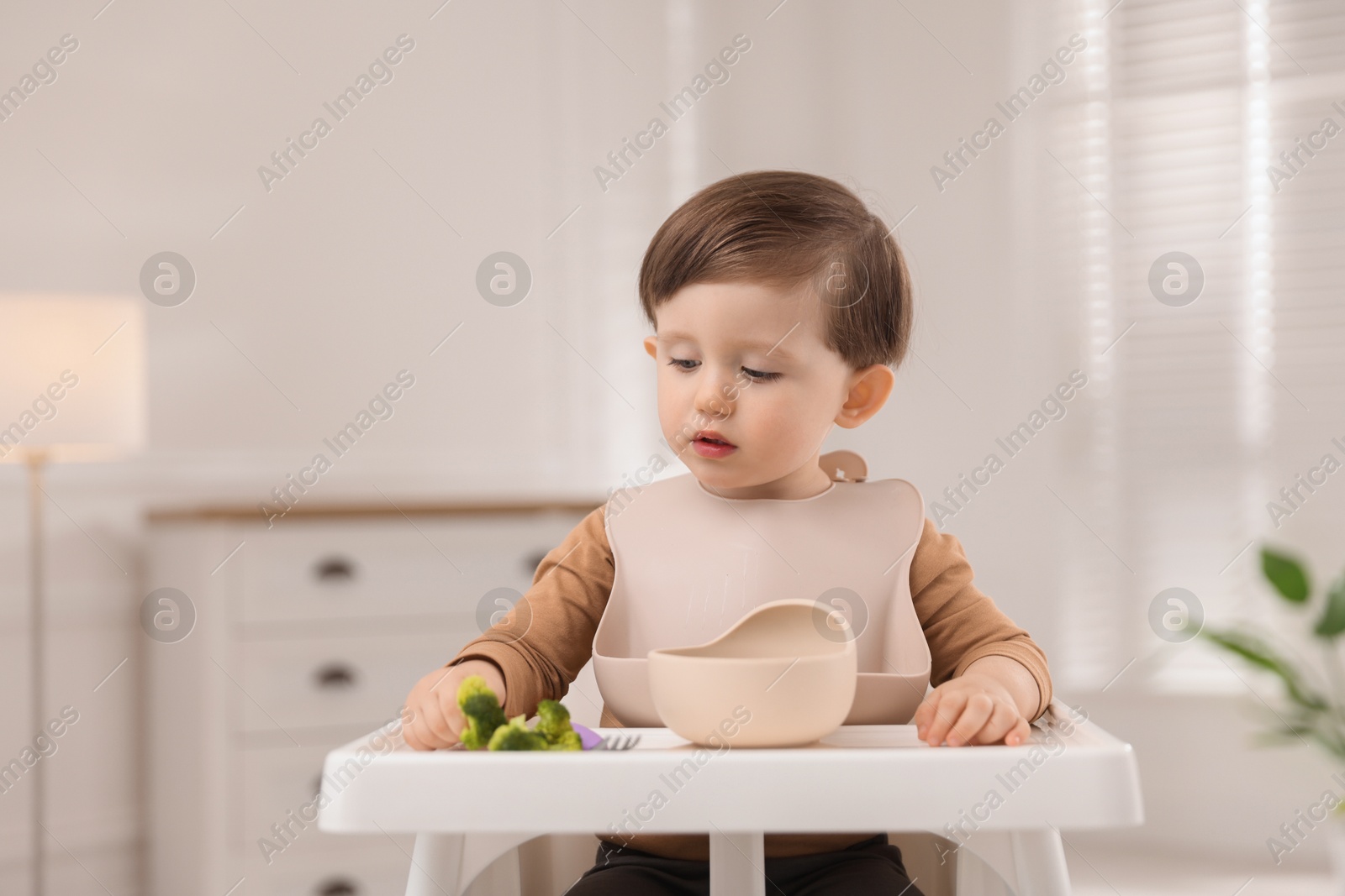 Photo of Cute little baby eating healthy food from bowl in high chair at home