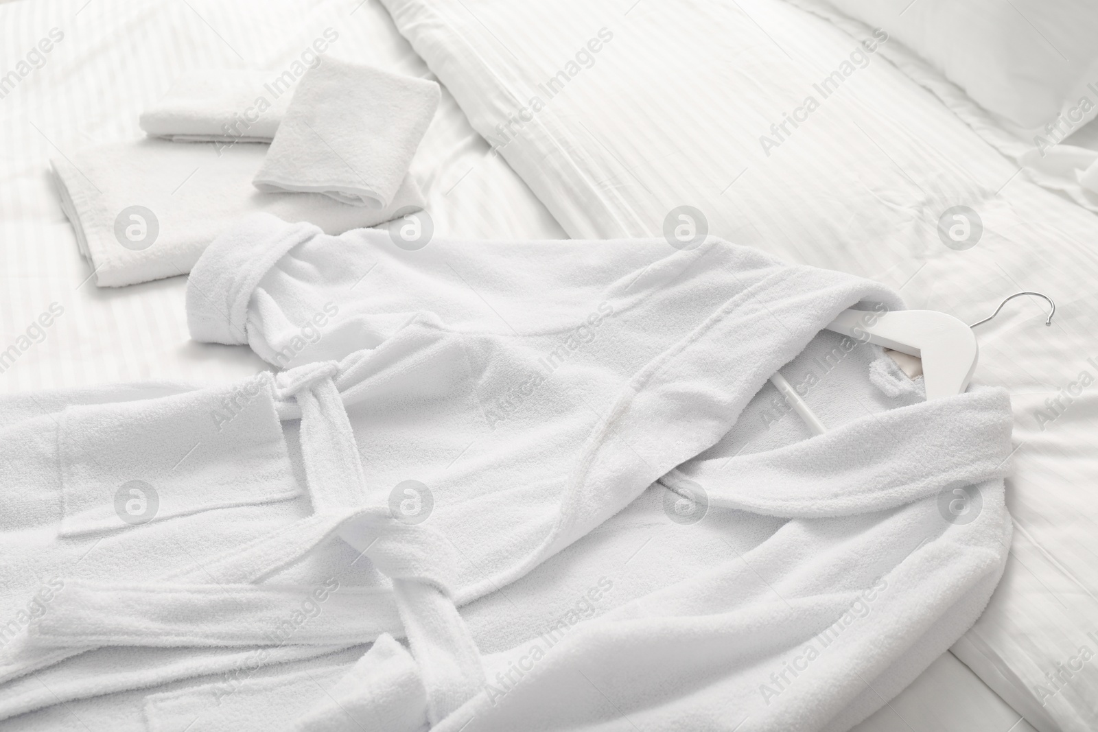 Photo of Bed with clean linens, towels and bathrobe indoors, closeup