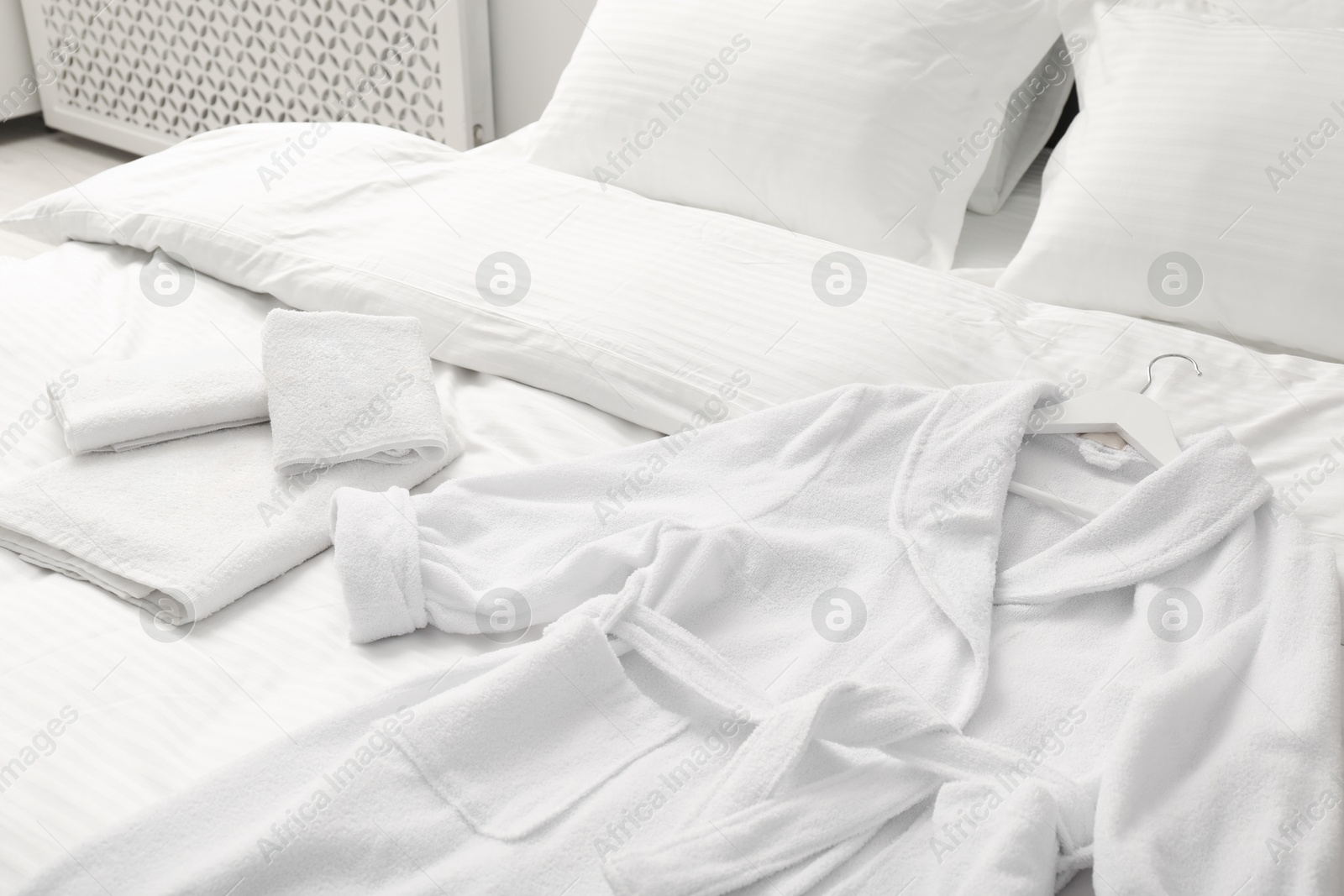 Photo of Bed with clean linens, pillows, towels and bathrobe indoors