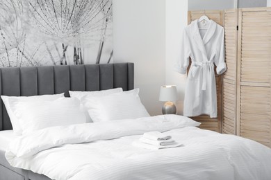 Photo of Bed with clean linens, pillows, towels and bathrobe indoors