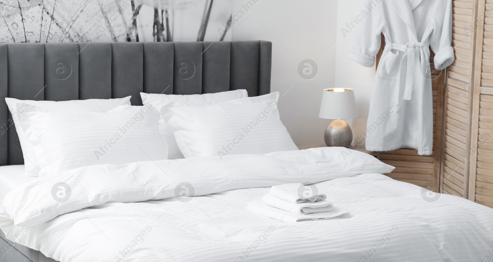 Photo of Bed with clean linens, pillows, towels and bathrobe indoors