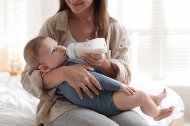 Photo of Mother feeding her little baby from bottle on bed indoors, closeup