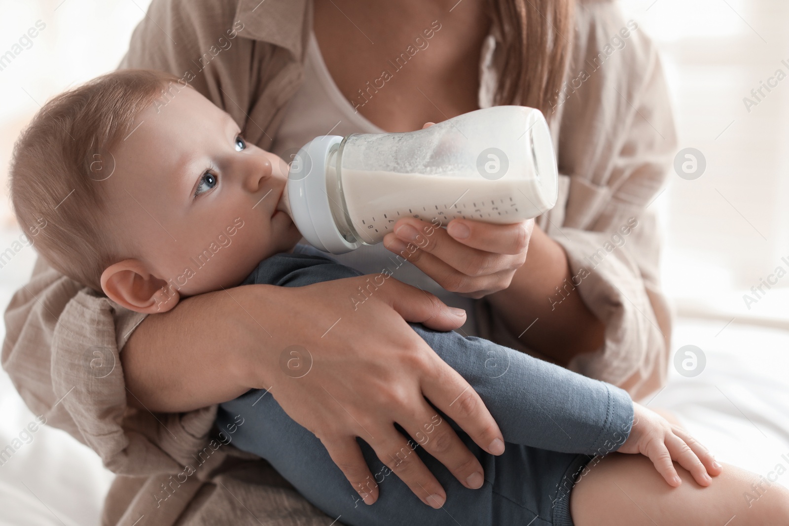 Photo of Mother feeding her little baby from bottle on bed indoors, closeup