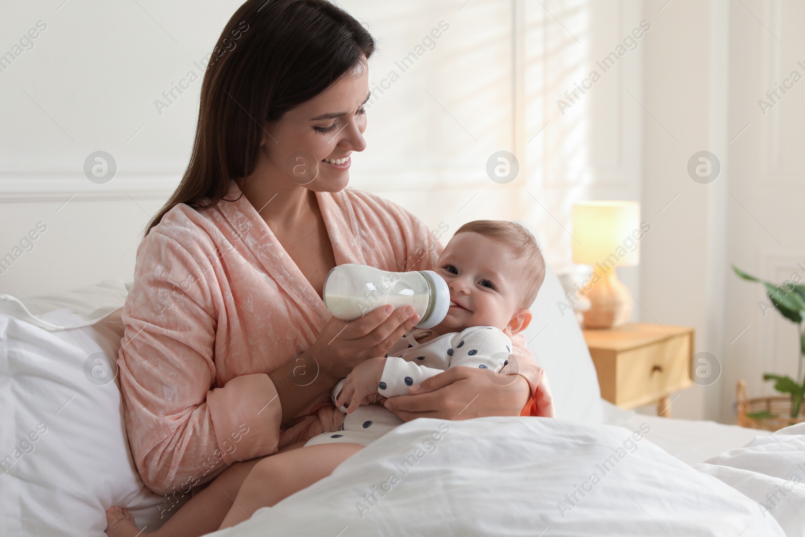 Photo of Mother feeding her little baby from bottle on bed at home