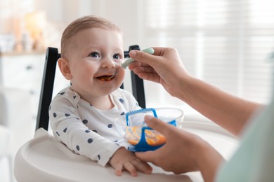 Photo of Mother feeding her cute little baby in high chair at home, closeup