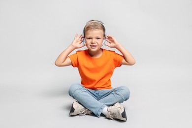 Little boy listening to music on light grey background