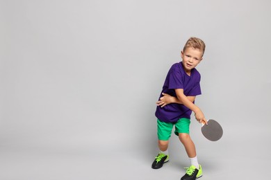 Photo of Little boy with ping pong racket on light grey background, space for text