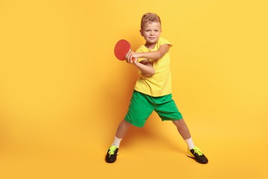 Photo of Little boy with ping pong racket on orange background, space for text