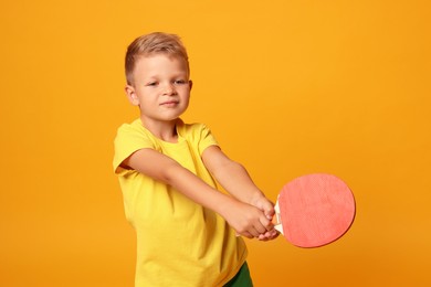 Photo of Little boy with ping pong racket on orange background