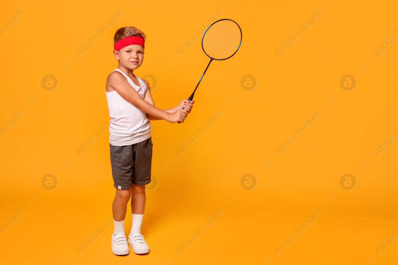 Photo of Little boy with badminton racket on orange background, space for text