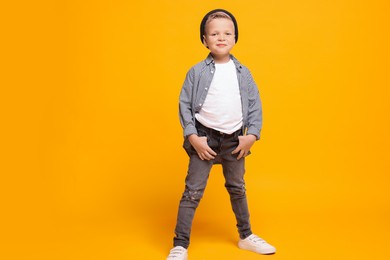 Full length portrait of little boy with stylish clothes on orange background