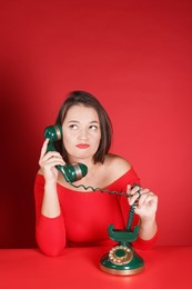 Photo of Woman talking on green vintage telephone against red background