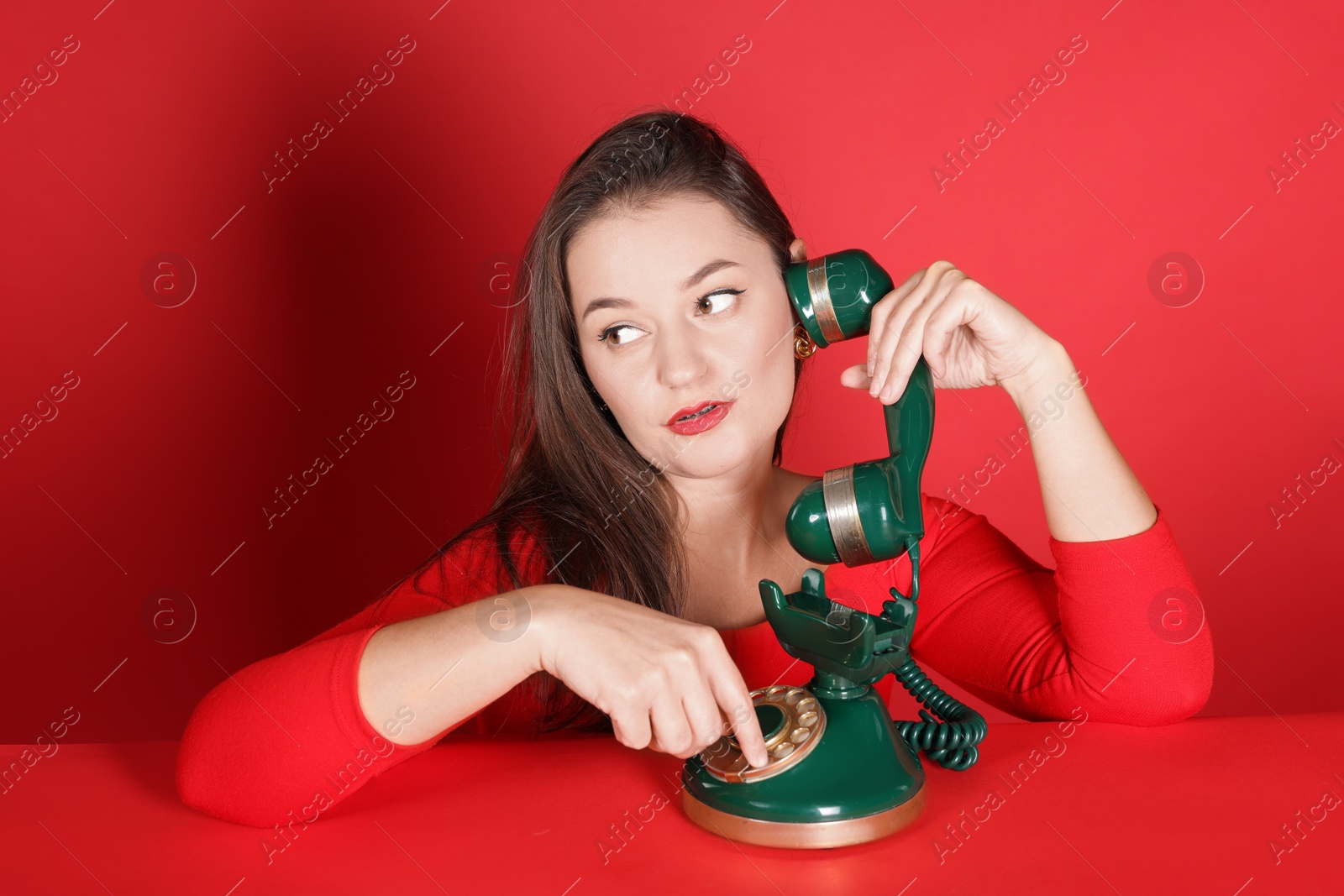 Photo of Woman talking on green vintage telephone against red background