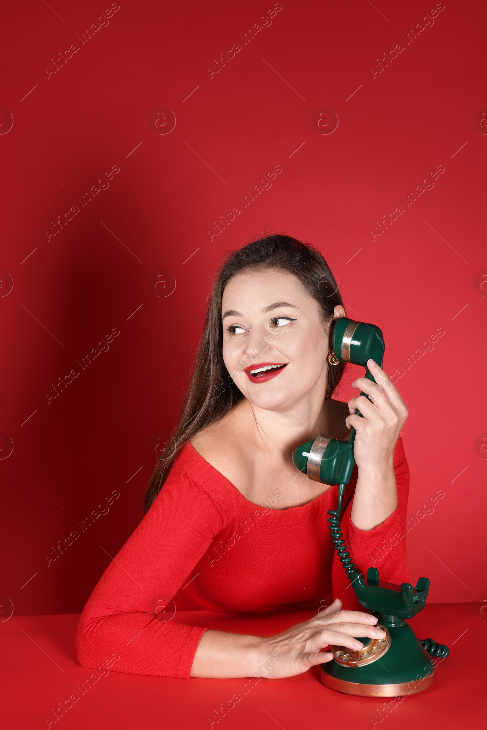 Photo of Woman talking on green vintage telephone against red background