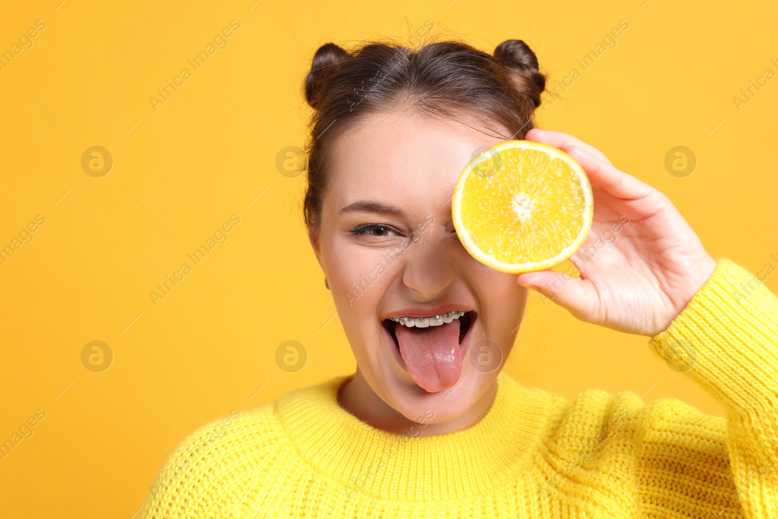 Photo of Happy girl holding orange half near eye on orange background