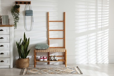 Photo of Stylish hallway interior with shoe storage bench, chest of drawers, houseplants and coat rack